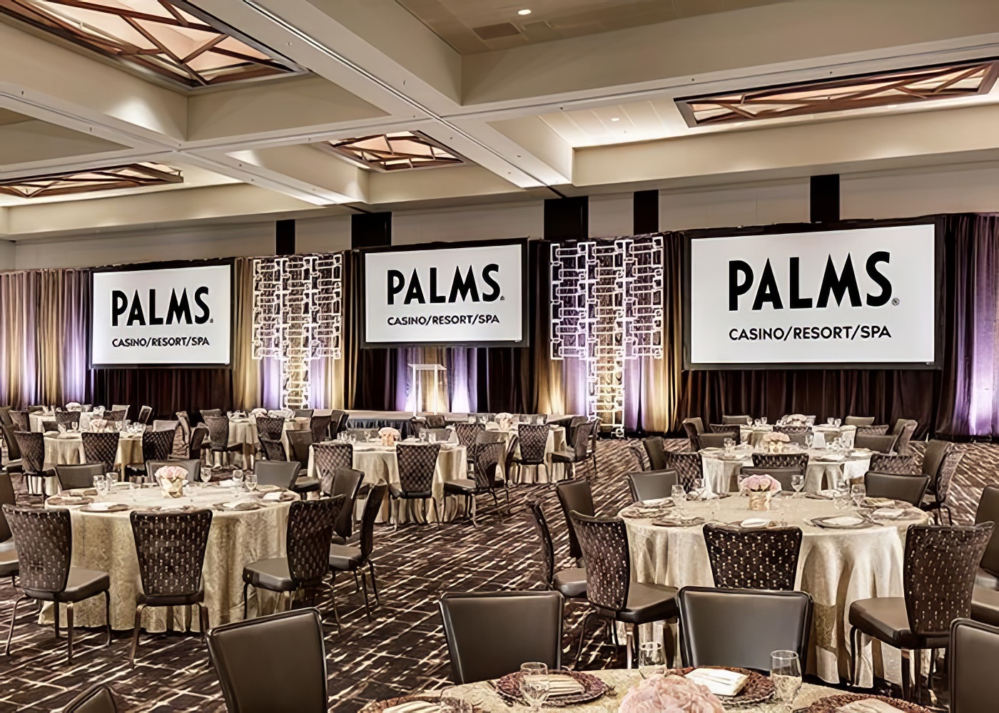Palms Casino Resort meeting space set for a banquet, round tables with ivory linens and three Palms-branded screens on stage.